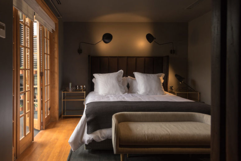 This is a master bedroom with an upholstered bed, a comfy bench, gilded touches and wall lamps