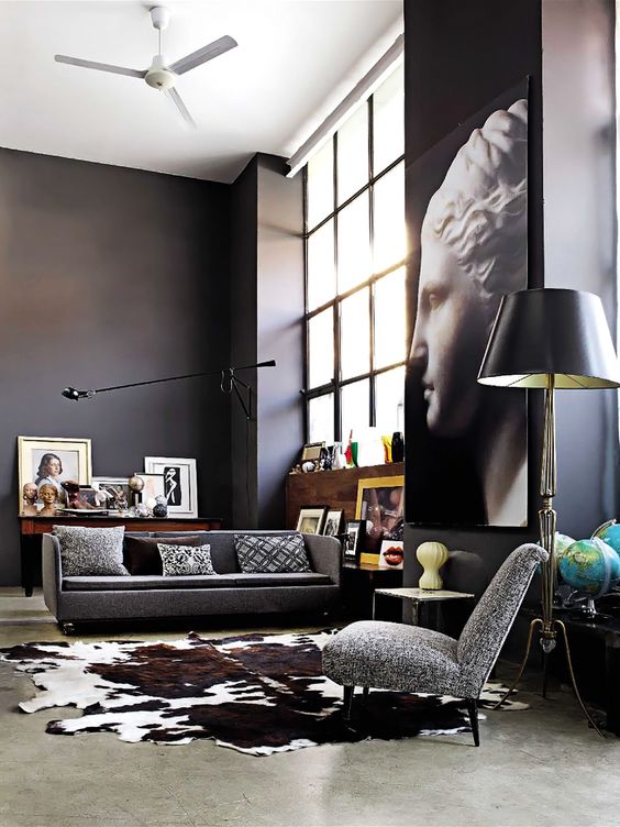 a gorgeous modern space with black walls, lots of artworks, big windows of double height and grey upholstery