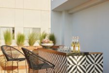 11 a modern outdoor bar clad with black and white geo tiles and a wooden countertop, a couple of black chairs