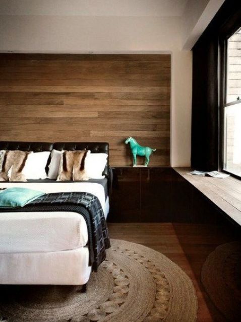 a modern bedroom with a wooden headboard wall, a wicker rug and a leather upholstered bed