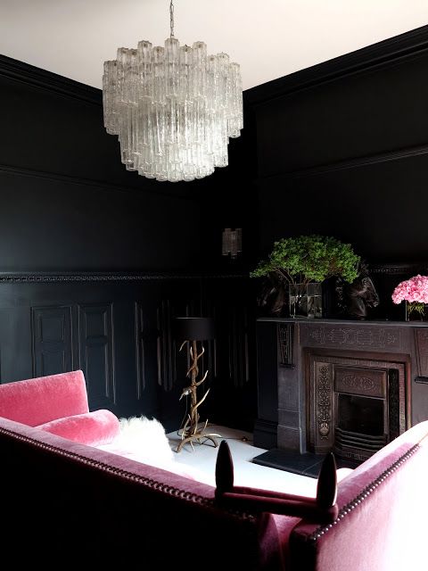 a luxurious moody living room with black walls, a crystal chandeliers, a pink sofa and a vintage fireplace