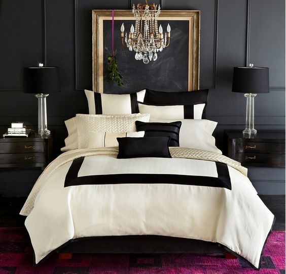 an elegant space with a black panel wall, black lamps and nightstands and a glam chandelier