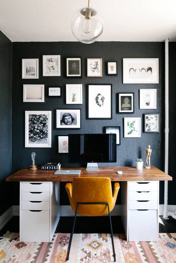 a modern home office with black walls, a gallery wall and a comfy desk with a wooden desktop