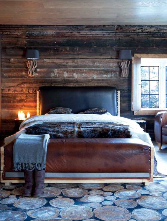 a cabin-inspired bedroom with a dark stained wooden wall, a leather bed and a rug that imitates wood slices