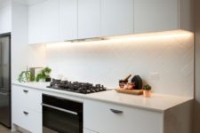 22 a modern white kitchen is made more eye-catchy with lights and a geometrically clad backsplash
