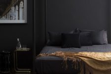 25 a moody bedroom with a framed black bed, black walls, bedding and some gold and brass touches here and there