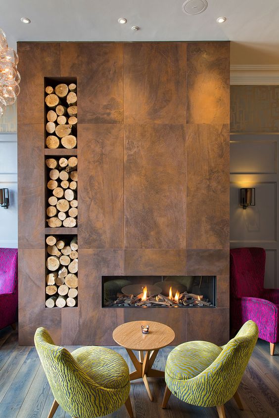 this beautiful fireplace is clad with tiles that imitate aged metal or wood, with a firewood storage
