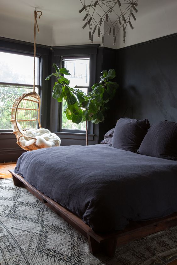 a welcoming space with black walls, a dark wooden bed and dark bedding is filled with light from several windows