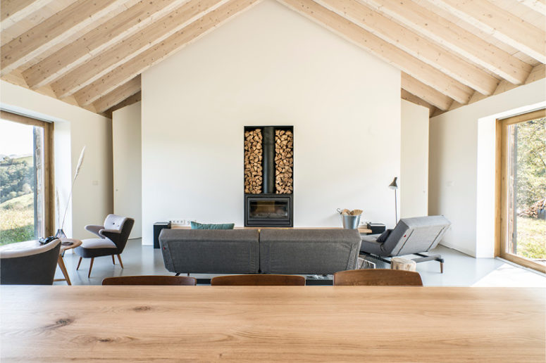 The living area features wooden beams on the ceiling, a wood stove, some comfy furniture and large windows to catch the views