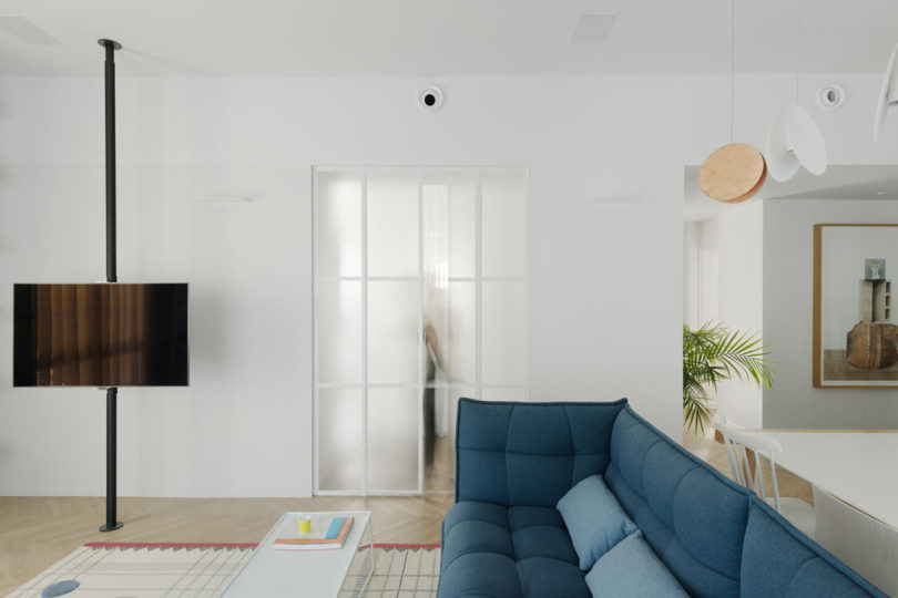The living room features a blue sofa, a suspended TV, the doors are made of frosted glass, which doesn't make space dividing so harsh and still separates them