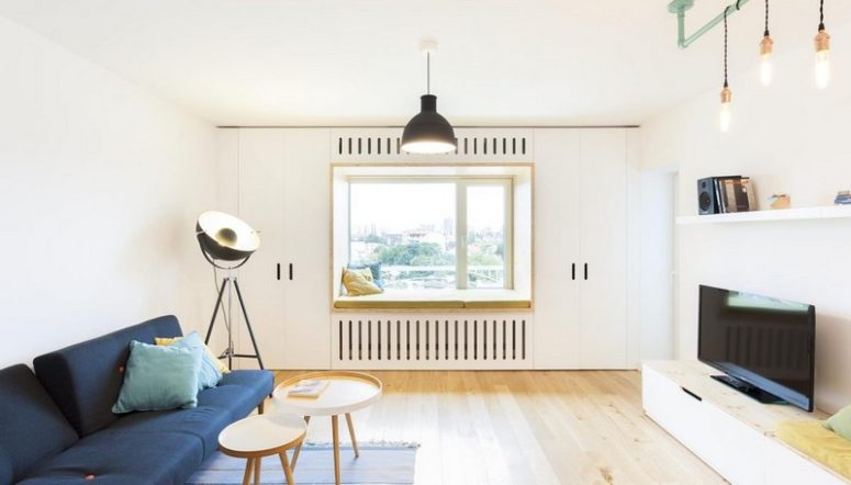 The living room is filled wiht light, there's a navy sofa, a storage and TV unit, some simple furniture and a window sill day bed