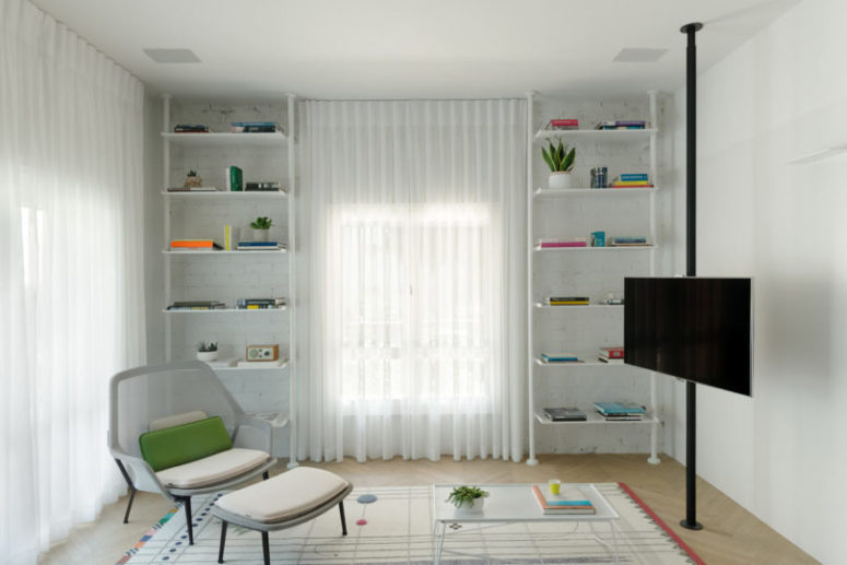 A whitewashed brick wall adds texture, there are open shelves and a comfy armchair with a footrest