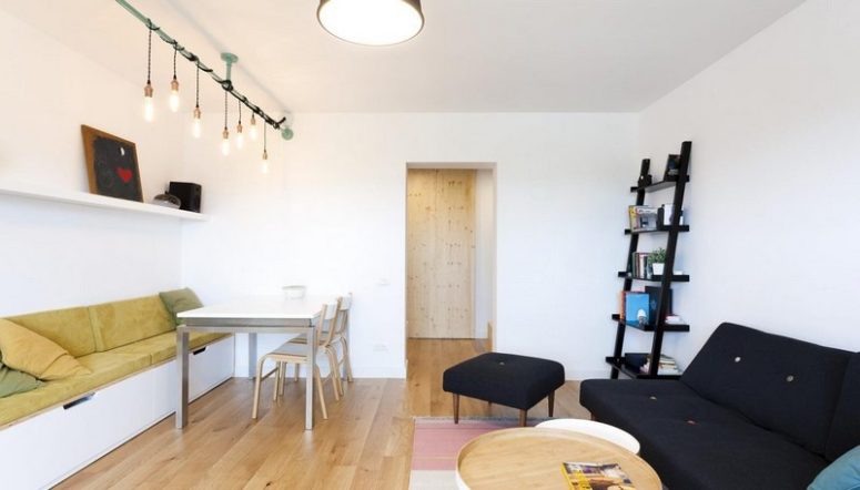 You can see light bulbs hanging from above and some comfy upholstered furniture, and a dining table next to the TV unit