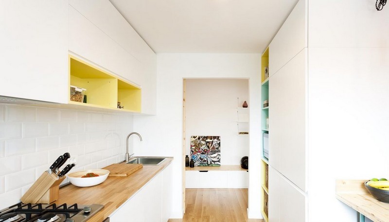 The kitchen is minimalist, with sleek white cabinets, colorful inside of cabinets, butcher's block tops