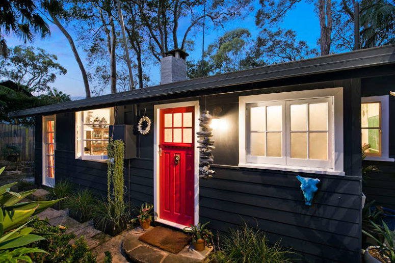 Outside the home is clad in black, there's a red door and some hangings from driftwood and shells as this is a beach home