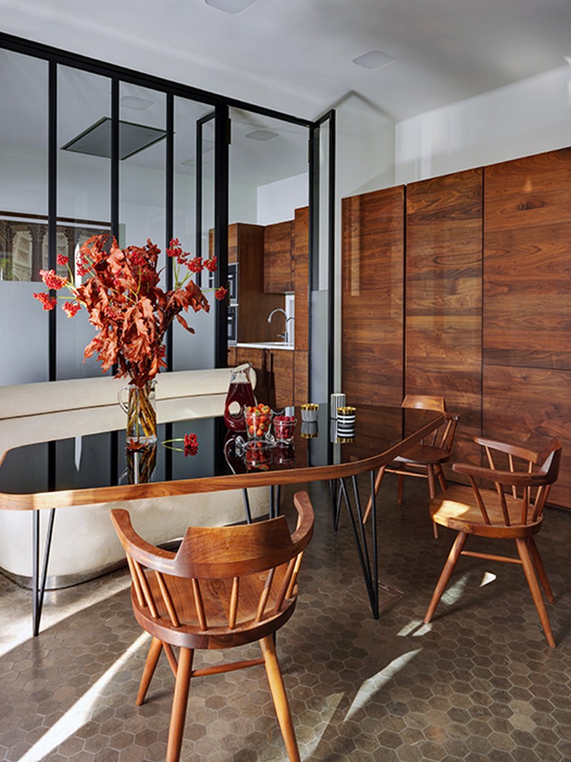 The dining space is done with a rich colored wood cupboard, chairs and a chic table with a black glass top