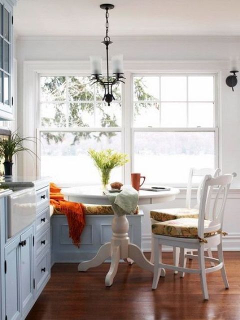 a cozy coastal breakfast space with a white pedestal table, some colorful printed chairs and a bench