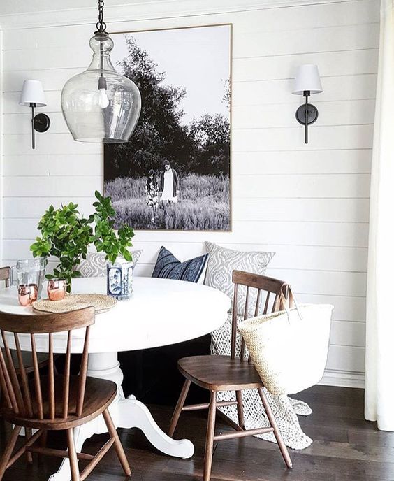 a cool farmhouse breakfast nook with a white pedestal table and some wood chairs looks very cozy and inviting