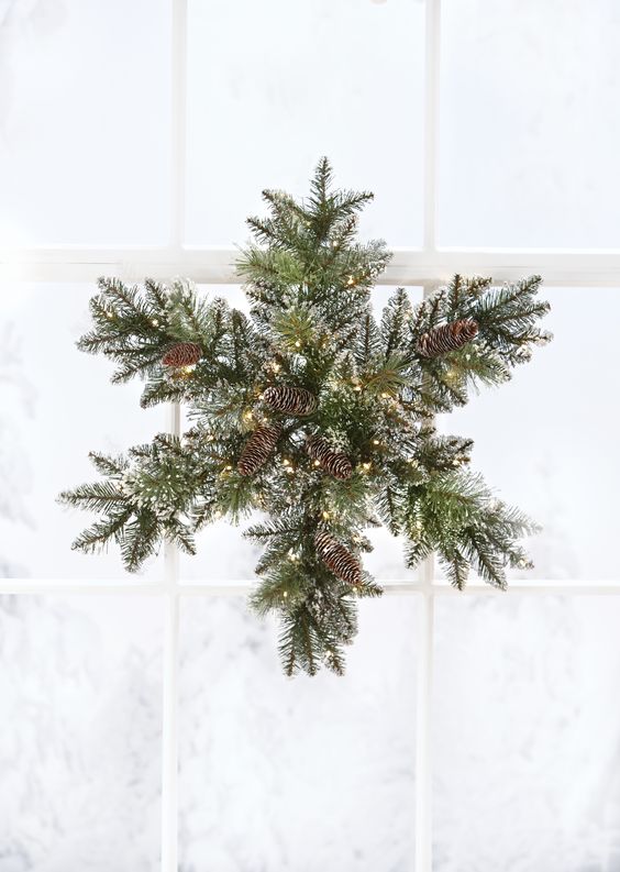 a snowy evergreen Christmas wreath with pinecones and lights shaped as a snowflake