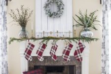10 plaid stockings, an evergreen garland with wooden beads, candles in gilded candle holders and a snowy wreath over the mantel