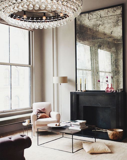 a large antique mirror over the fireplace and a large crystal chandelier for a refined glam space