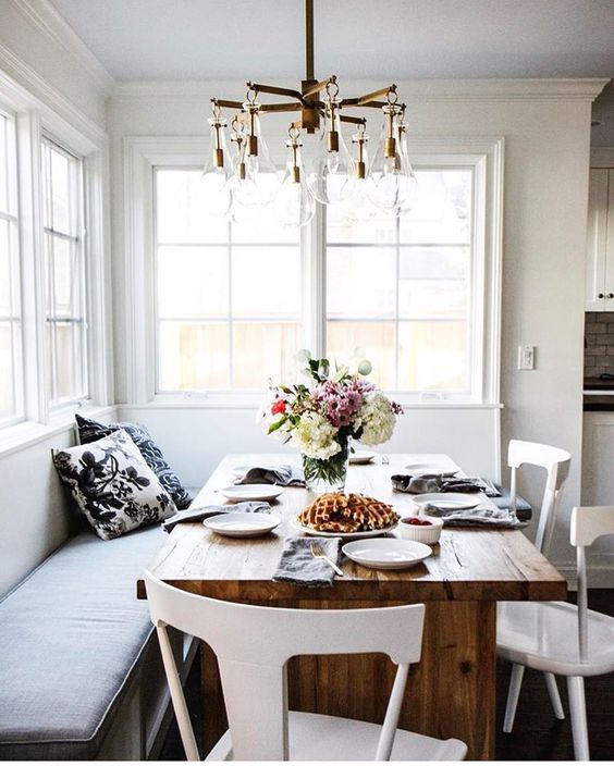 a chic breakfast nook or dining space with a corner sofa and a wooden table is filled with natural light