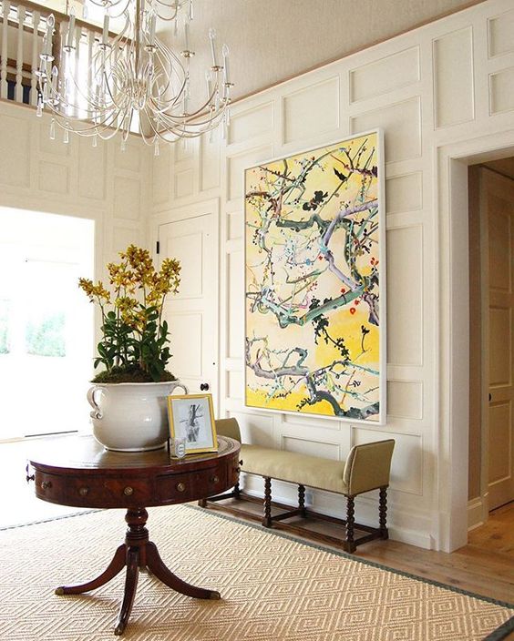 a refined entryway with a vintage pedestal round table, a large pot with flowers and an artwork