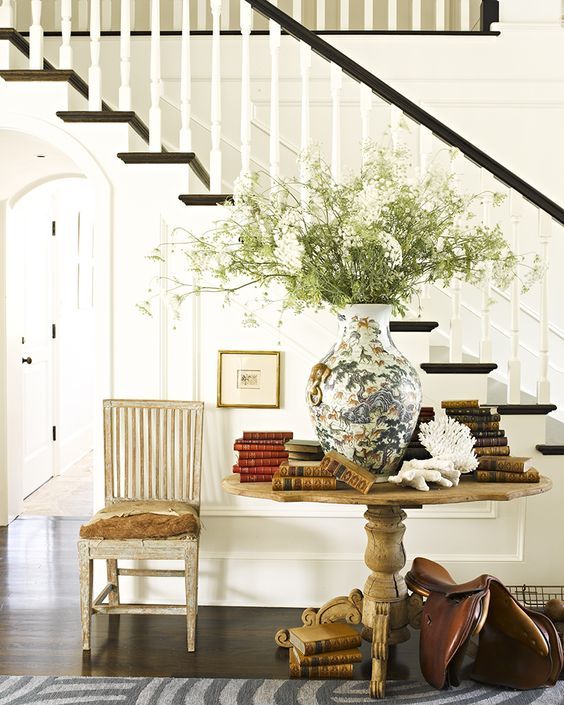 a vintage wooden pedestal table with lots of books and a large vase with greenery looks wow