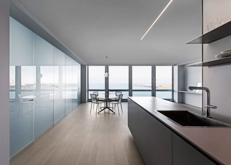 The kitchen features simple grey cabinets, there's a dining zone by the glazed wall. which is done with some translucent chairs and a glass table