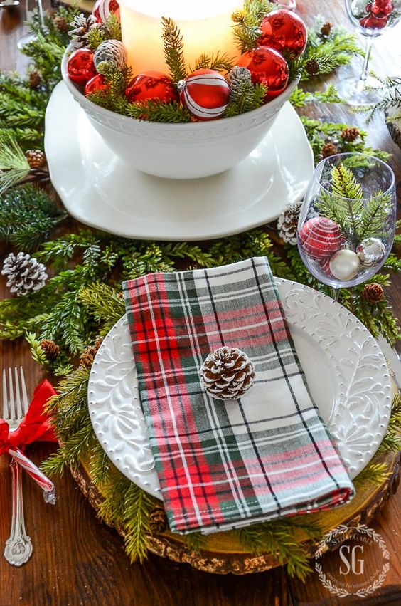 a cozy traditional table setting with evergreens, pinecones, plaid napkins and ornaments