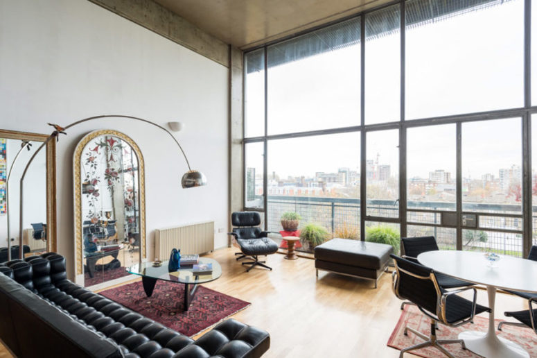 The living room is done with black leather furniture, several coffee tables and eye-catchy vintage mirrors, it's flooded wit light through a glazed wall