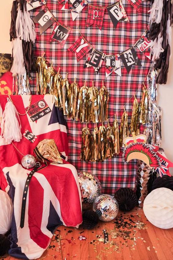 a colorful and cheerful photo booth with banners, a plaid backdrop, disco balls and fringe tassels