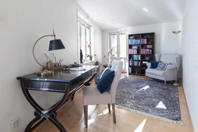 This is a workspace with a vintage desk, a bookcase and some comfy chairs and artworks