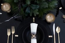 05 a black table with black plates and cahrgers, lsuh evergreens and gold cutlery for a moody tablescape