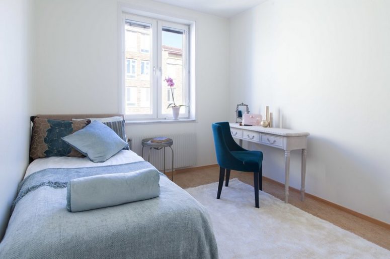 The bedroom is done with an upholstered bed, a vintage dressing table and a dark velvet chair