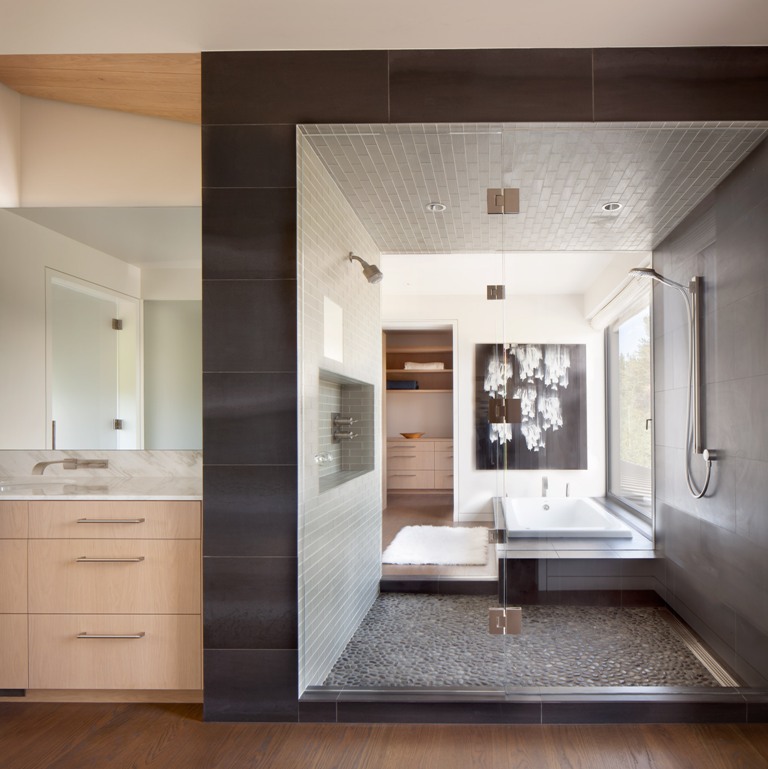 This is a bathroom done with various kinds of tiles, wood and some pebbles on the floor for a natural feel