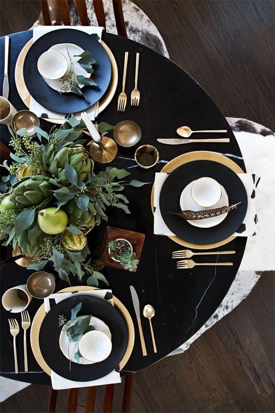 a black table, black and gold plates, a lush greenery, veggies and pears centerpiece