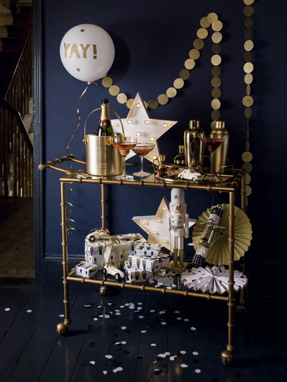 a brass bar cart with a gold garland, a neon star sign, paper fans and a balloon