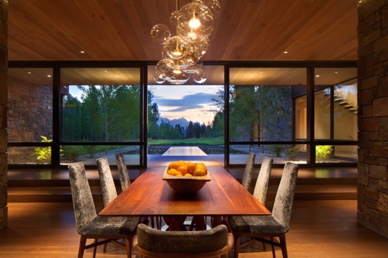 The dining space features grey velvet chairs, a dining table, some glass bubble lamps and breathtaking views
