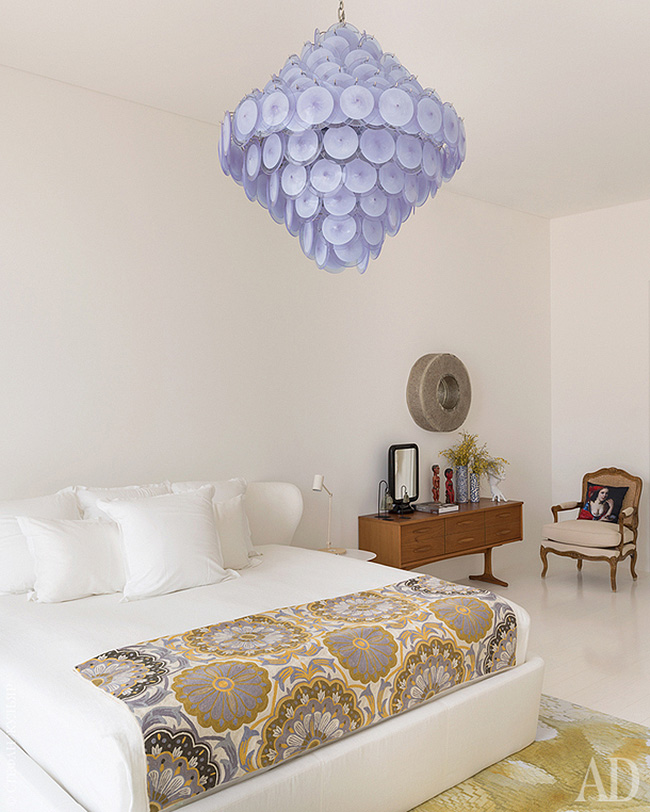 The master bedroom is done with an upholstered bed, a lavender disc chandelier and some vintage furniture