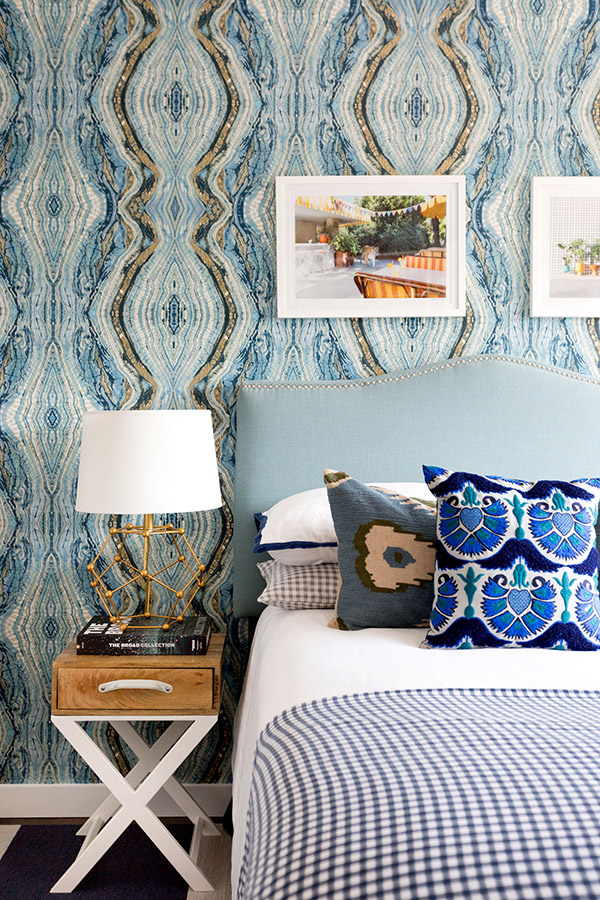The master bedroom is decorated in blue hues, with geode print wallpaper, wooden nightstands and some photos