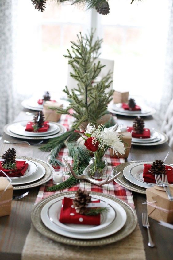 a cozy rustic table setting with a plaid runner, antlers, evergreens and pinecones for each place setting