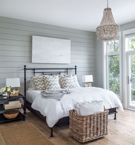 a rustic bedroom with a gla feel and a large basket at the foot of the bed for storing pillows