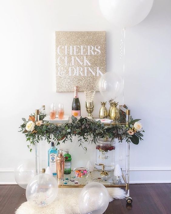 a chic bar cart decorated with a greenery garland and blooms and gold pineapple ice holders