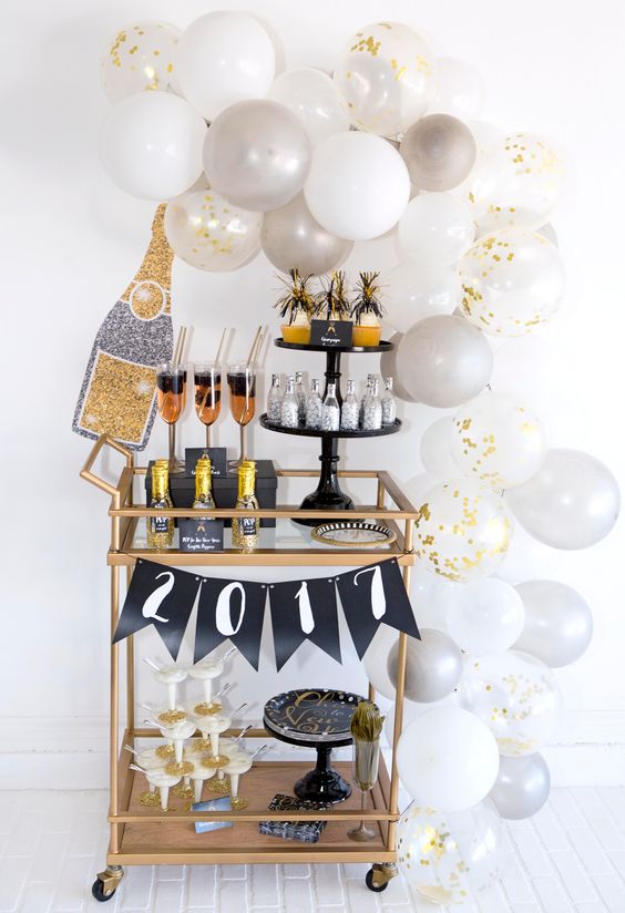 a copper bar cart with white and grey balloons, a banner and glitter bottles and glasses