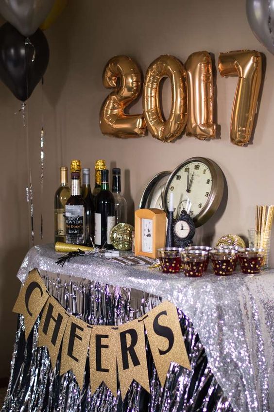 a drink station decorated with silver fringe, a glitter garlands, gold balloons and disco balls