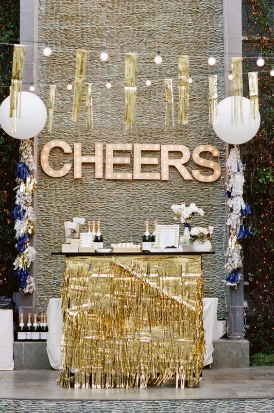 a drink station with gold fringe, gold fringe garlands and marquee lights