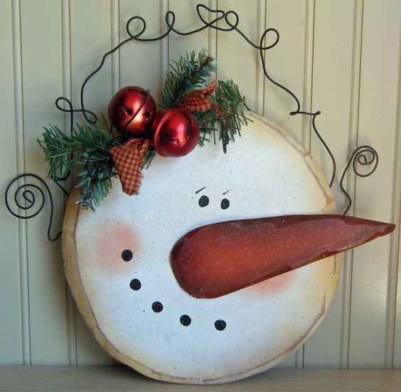 a large snoman face wood slice sign with evergreens, bells and a plaid ribbon piece
