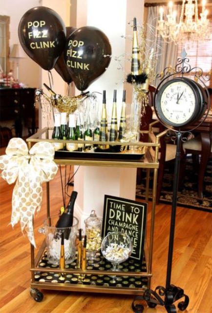 a stylish drink bar cart in black and gold with black and gold balloons and a large bow