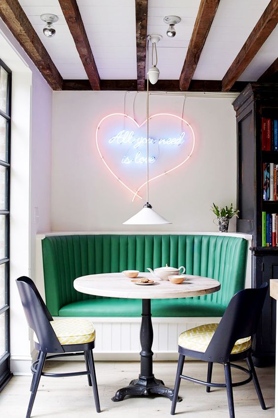 a chic retro diner breakfast nook with a neon sign, an emerald sofa and printed chairs
